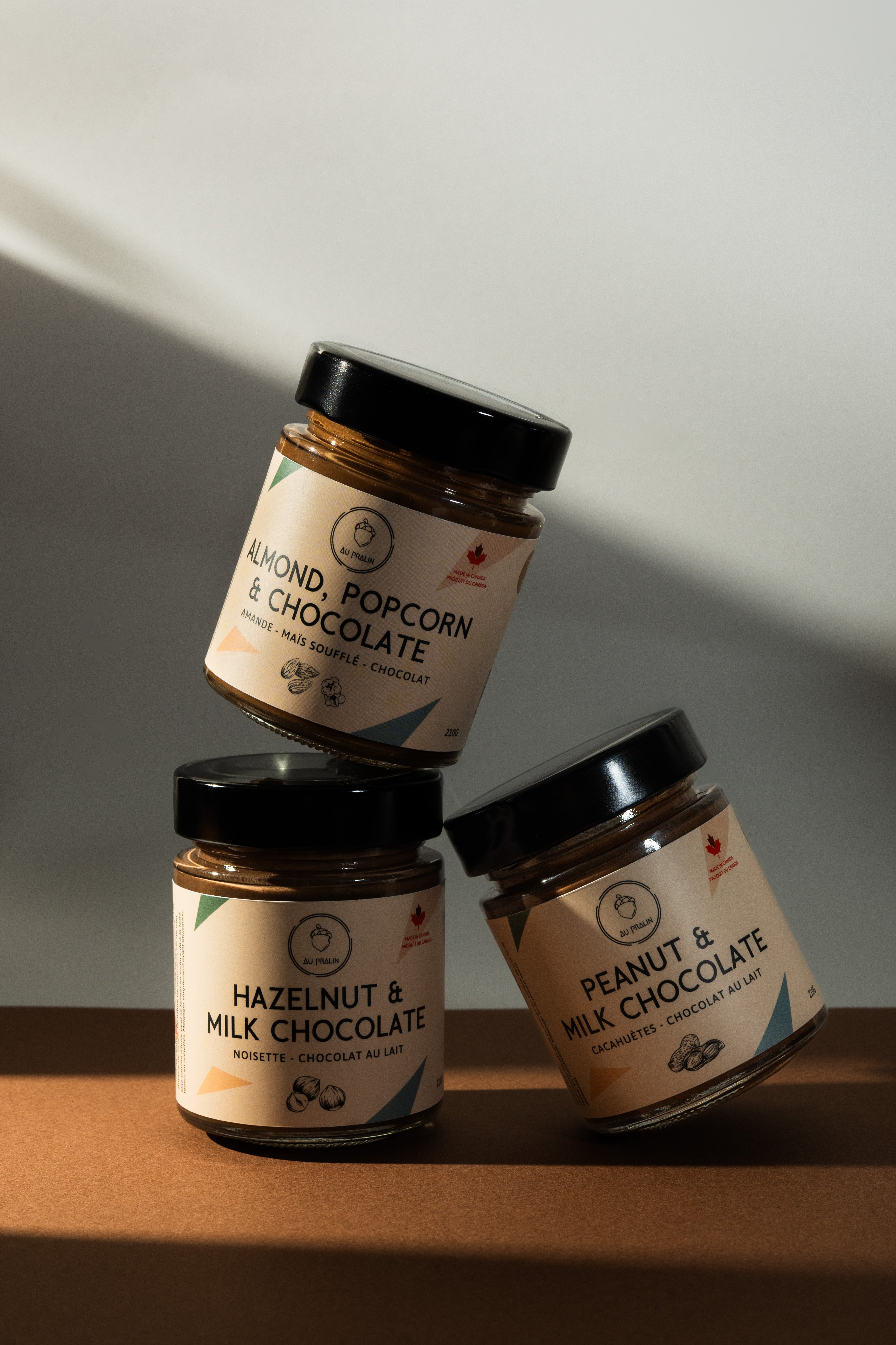 Three jars of chocolate spreads/nut butters stacked on a wooden surface with a neutral background